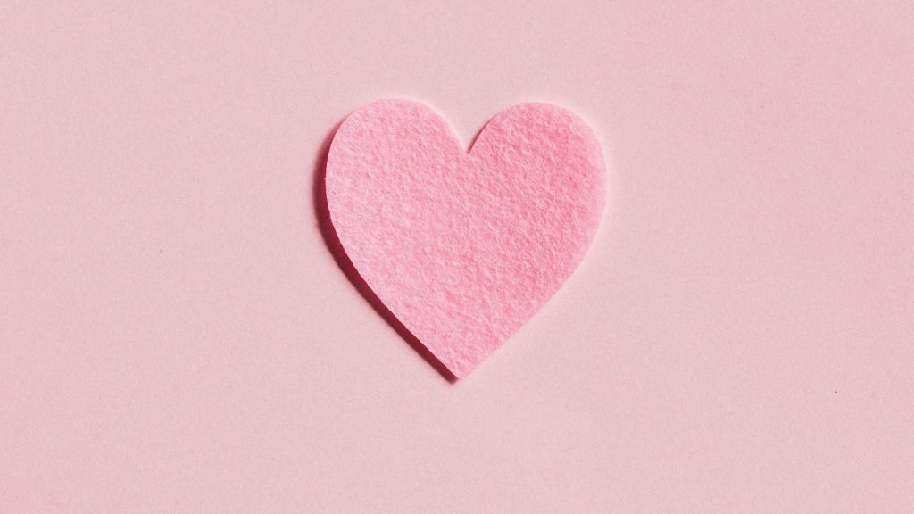 A simple pink felt heart on a light pink background, perfect for Valentine's Day themes.