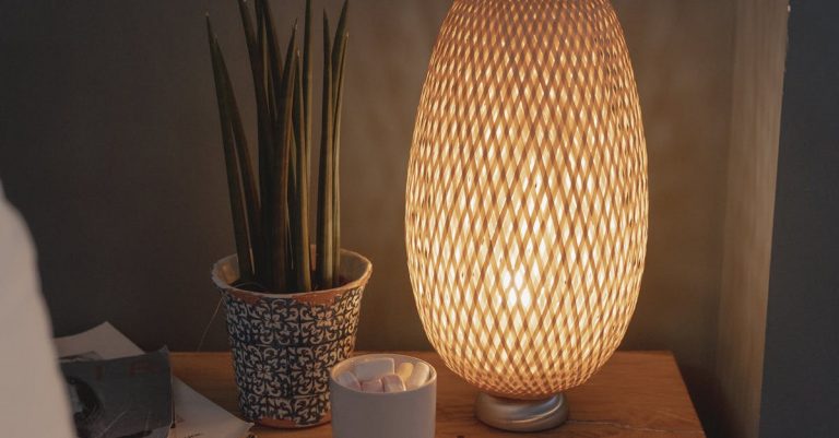 A warm, beautifully lit nightstand featuring a woven lamp and potted plant, creating a cozy atmosphere.